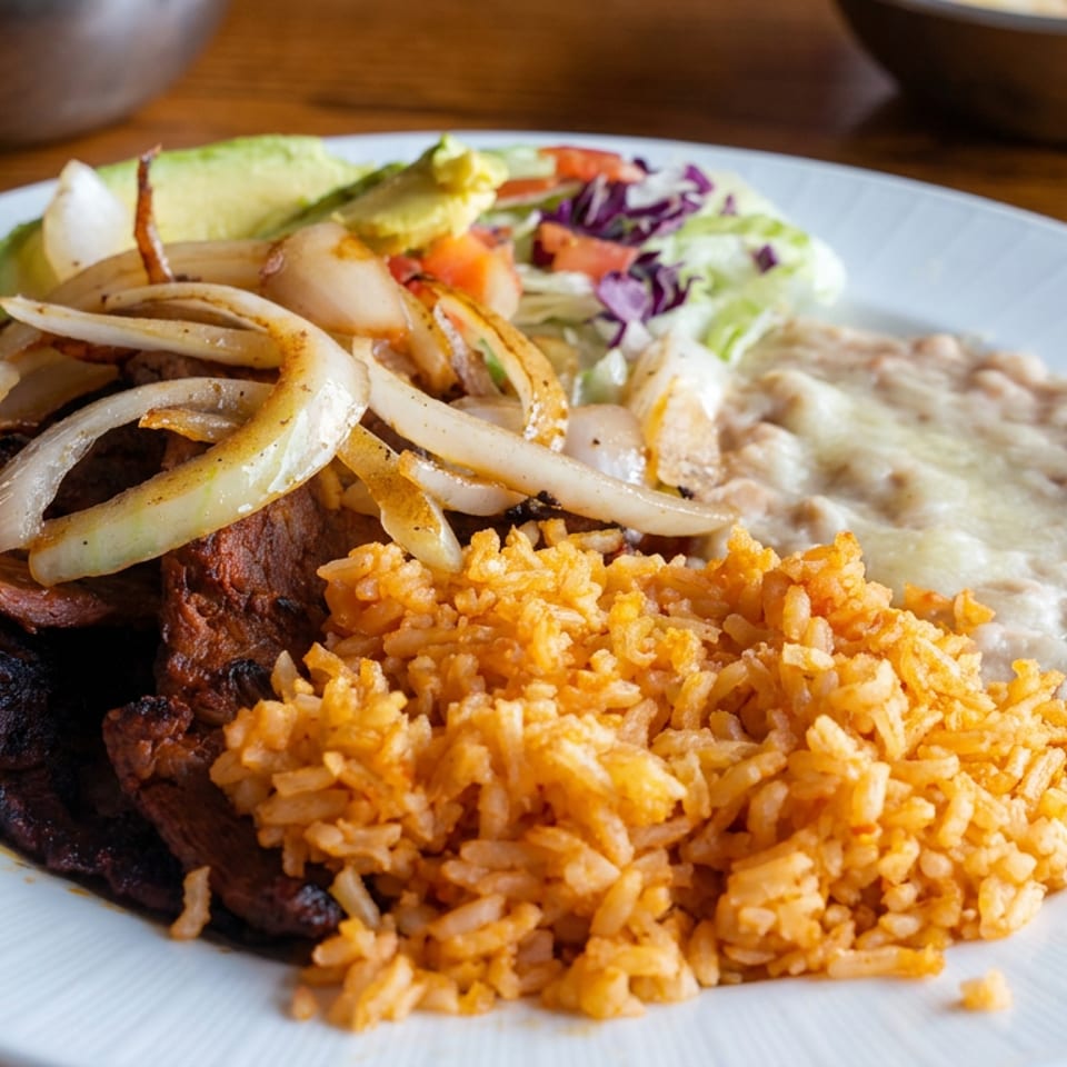 Plate of grilled steak topped with onions, Mexican rice, refried beans, avocado, and fresh cabbage salad.